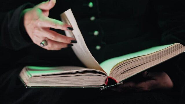 Hands of black witch woman turns over pages of old magic book. Magician learns spells, rituals, esoteric halloween cosplay concept.