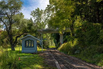 A small building, not much larger than an outhouse, stands beside a train track through a forest...