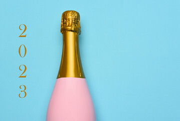New Years 2023 Concept. A Pink Champagne bottle on a blue teal background, with the text 2023 on...