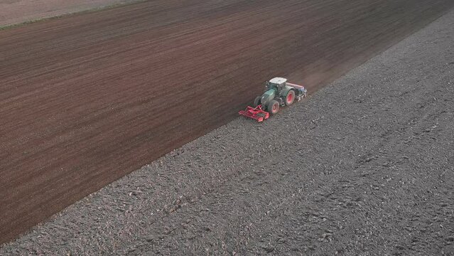 Farm tractor harrowing field. Tractor with harrow system plowing ground
