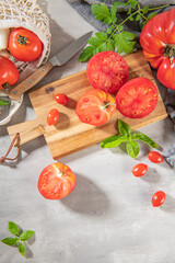 Large variety of tomatoes on rustic kitchen counter. Preparation of tomato sauce with onions and basil