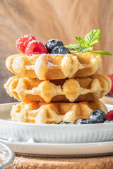 Traditional Belgian waffles stacked with fresh raspberries and blueberries sprinkled with powdered sugar on the kitchen counter