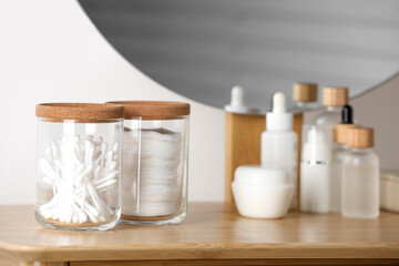 Fototapeta na wymiar Glass jars with cotton swabs and pads near cosmetic products on dressing table