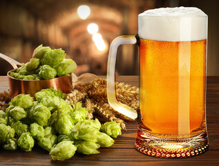 Glass of tasty light beer, fresh hops and wheat spikes on wooden table in cellar