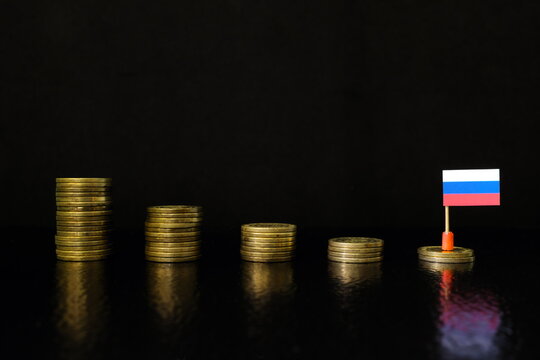 Russia economic recession, financial crisis and currency depreciation concept. Russian flag in decreasing stack of coins in dark black background.