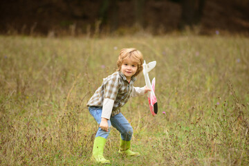Child pilot with toy airplane dreams of traveling in summer in nature. Kids dreams. Kid having fun with toy airplane in field. Childhood dream imagination concept.