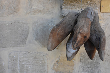 Antique  wooden cobbler  shoe molds needed to make shoes hang on an old stone wall. Shoe Making Repairing