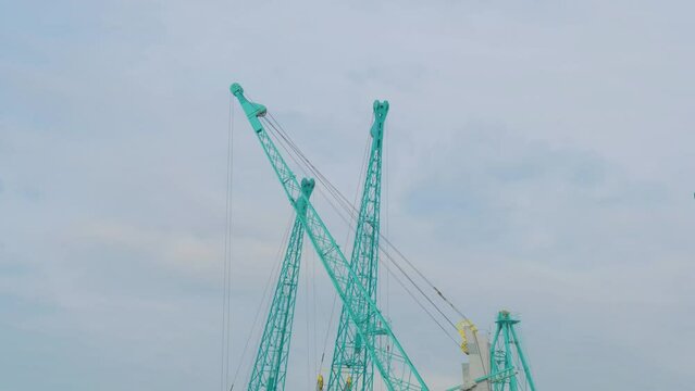 Three harbor cranes during work against the cloudy sky in the sea cargo port. Industrial, transportation, loading and machinery concept