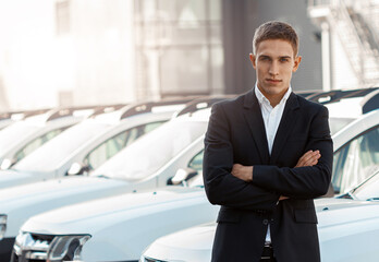 Young male consultant in auto show standing near cars and looking at camera