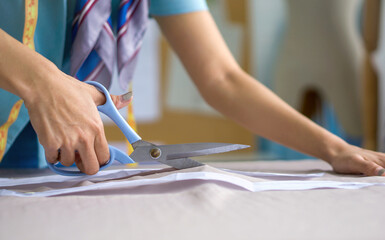Closeup dressmaker hand use scissors to cut fine beige fabric.