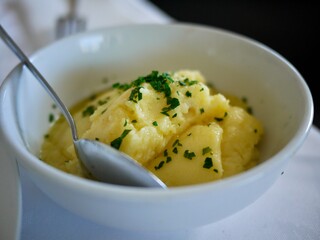 smashed potato with parsely and spoon in a white fine chain bowl