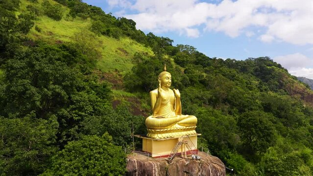 Aerial drone of statue of the golden Buddha in a mountain Buddhist temple. Aluvihara Rock Temple, Matale, Central Province, Sri Lanka