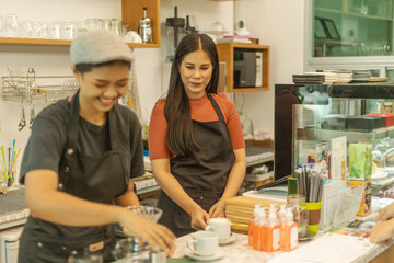 Female business owner works with her partner to prepare coffee or drink for customer in a coffee shop. A couple of LGBT startup help each other at a coffee counter for their business.