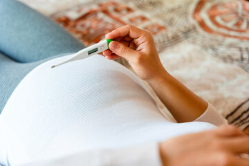 Pregnant thermometer temperature check. Pregnancy woman holding thermometer, check fever flu temperature. Pregnant girl sick. Concept of pregnancy, maternity, expectation for baby birth.
