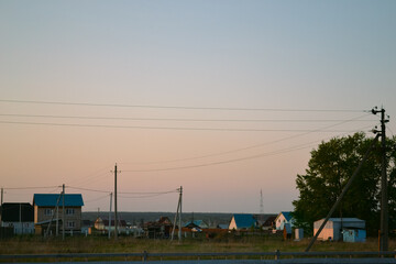 Fototapeta na wymiar A beautiful rural landscape with houses and power lines against the background of an evening clear sky