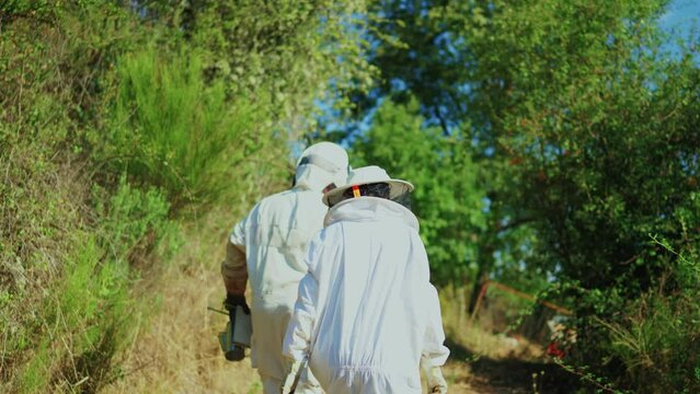 Two protected beekeepers walk to an apiary