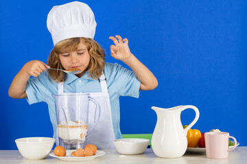 Kid boy in chef hat and apron cooking preparing meal. Little cook with vegetables at kitchen. Natural kids food.