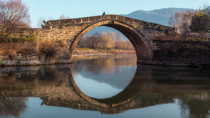 An old bridge over the reflecting water, at dawn in the fall of Yunan Province, China.