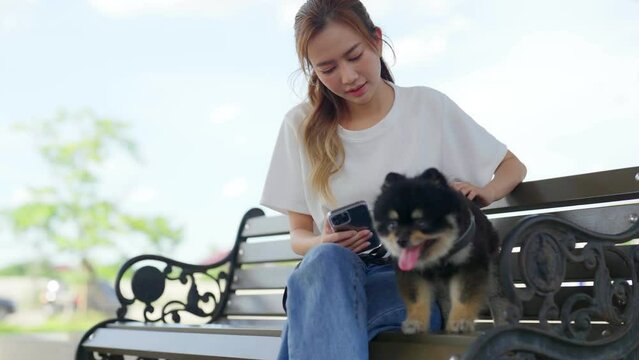 Happy young asian woman sitting on a bench and photo selfie in the park with her dog. Pet lover concept