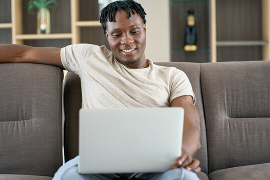 African american smile and sitting on safo and use laptop in home living room
