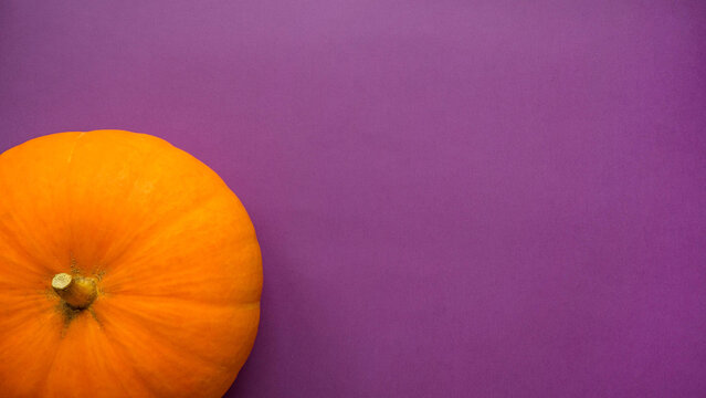 Orange pumpkin on purple background with space for text top view