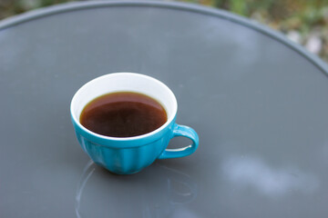 Big blue cup of hot coffee isolated on the gray table in the autumn morning garden. Top view.