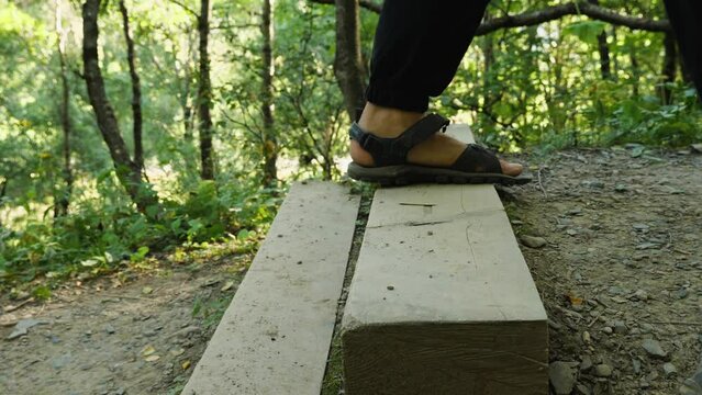Men's feet in black pants and black trekking sandals climb the wooden stairs in the woods. Side view. Close-up. Outdoor activities