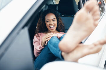 Portrait of woman with feet out window of car, sitting with smile on face. Travel, freedom and...