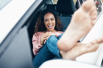 Portrait of woman with feet out window of car, sitting with smile on face. Travel, freedom and weekend holiday on a road for adventure. Young girl, barefoot and happy on roadtrip for summer vacation