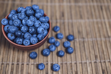 Fresh blueberries in a clay bowl. Bamboo mat, space for text.