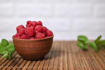 Fresh juicy organic raspberries in a clay bowl. Bamboo mat, green sprig of mint, space for text.