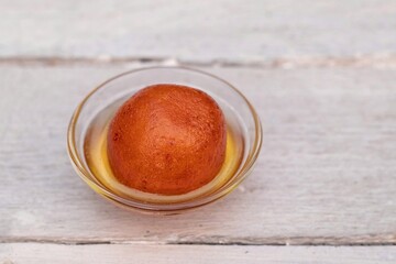 Closeup of Indian Gulab Jamun Sweets Served in a Small Glass Bowl with Sugar Syrup Isolated White Wooden Background with Copy Space