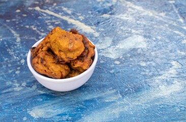 Closeup of Masoor Dal Pakoda or Red Lentil Vada in a White Bowl Isolated on Bluish Background with Copy Space