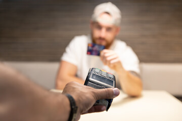 A young man is debating whether to use a credit card or cryptocurrency for payment. Card payment versus bitcoin.