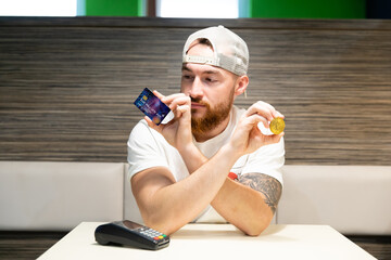 A young man is debating whether to use a credit card or cryptocurrency for payment. Card payment versus bitcoin.