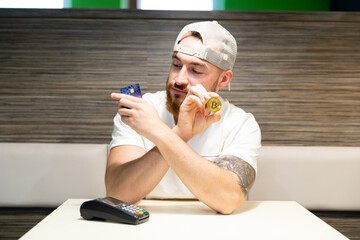 A young man is debating whether to use a credit card or cryptocurrency for payment. Card payment versus bitcoin.