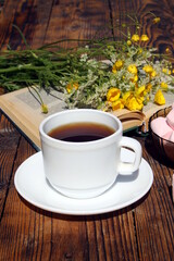 A cup of tea stands on a table with a bouquet of wild flowers under the summer rays of the sun.