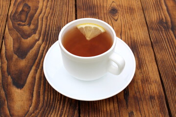 A cup of tea with lemon stands on a wooden table.