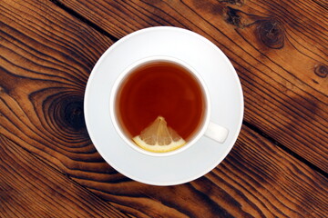 A cup of tea with lemon stands on a wooden table.