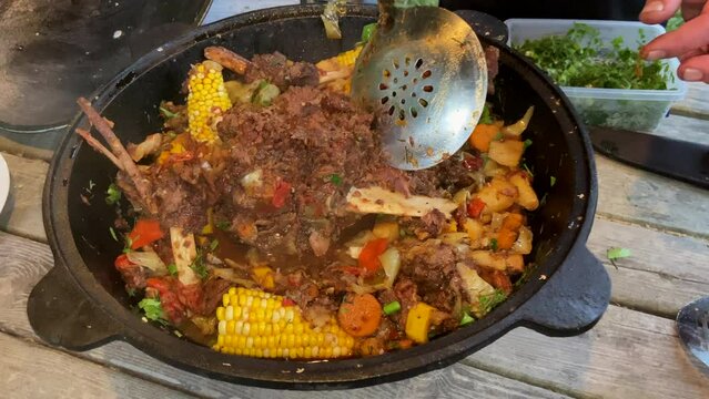 Corn with beef and vegetables. Shurpa in a cauldron. Tomato, red pepper and lamb soup cooked on hot coals. Hot beef hunting goulash or bograch soup with corn cobs, paprika, vegetables and spices.