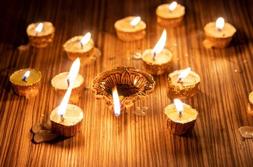 Happy Diwali or Deepavali Festival Diya with Glowing Lit Flame or Oil Lamp amid Burning Candles Isolated on Wooden Table, Deepavali or Diwali Festival Celebration Conceptual, Perfect for Wallpaper