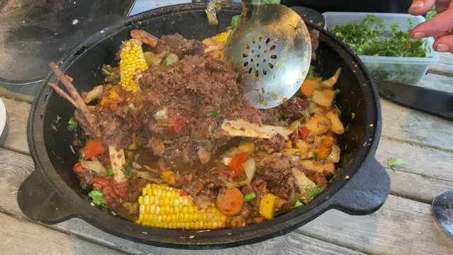 Corn with beef and vegetables. Shurpa in a cauldron. Tomato, red pepper and lamb soup cooked on hot coals. Hot beef hunting goulash or bograch soup with corn cobs, paprika, vegetables and spices.