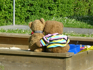 zwei süsse teddybären sitzen engumschlungen auf einer Sandkiste