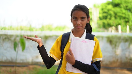 Smiling student girl wearing school backpack and holding exercise book. Portrait of happy asian young girl outside the primary school. Closeup face of smiling hispanic schoolgirl looking at camera.