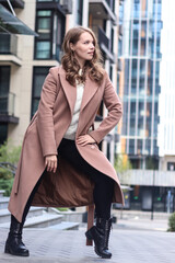 Obraz premium Street photo session of a girl with blond long hair in a beige coat. Photo shoot in the big city.