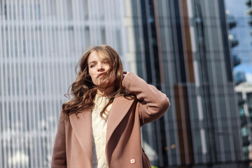 Street photo session of a girl with blond long hair in a beige coat. Photo shoot in the big city.