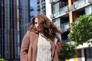 Street photo session of a girl with blond long hair in a beige coat. Photo shoot in the big city.