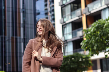 Street photo session of a girl with blond long hair in a beige coat. Photo shoot in the big city.
