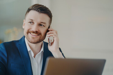Happy young handsome businessman talking on mobile phone with partner in front of laptop