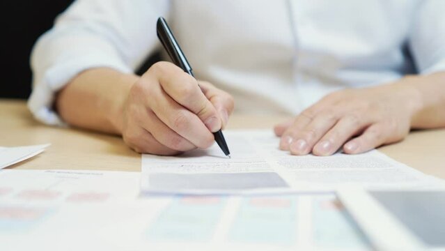 close-up of man hands filling out a questionnaire or document signs Business Contract Or Agreement at table in office. Asian employee writes a statement, questionary declaration at desk. Closeup